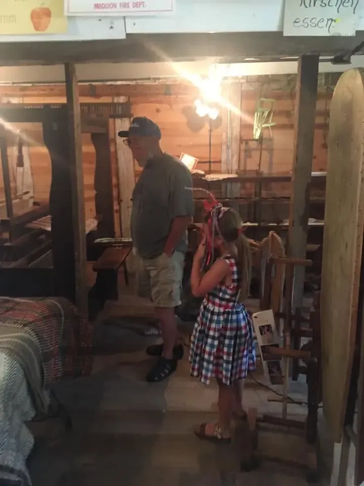 An older visitor and a young girl among the museum exhibits, an antique loom at the left