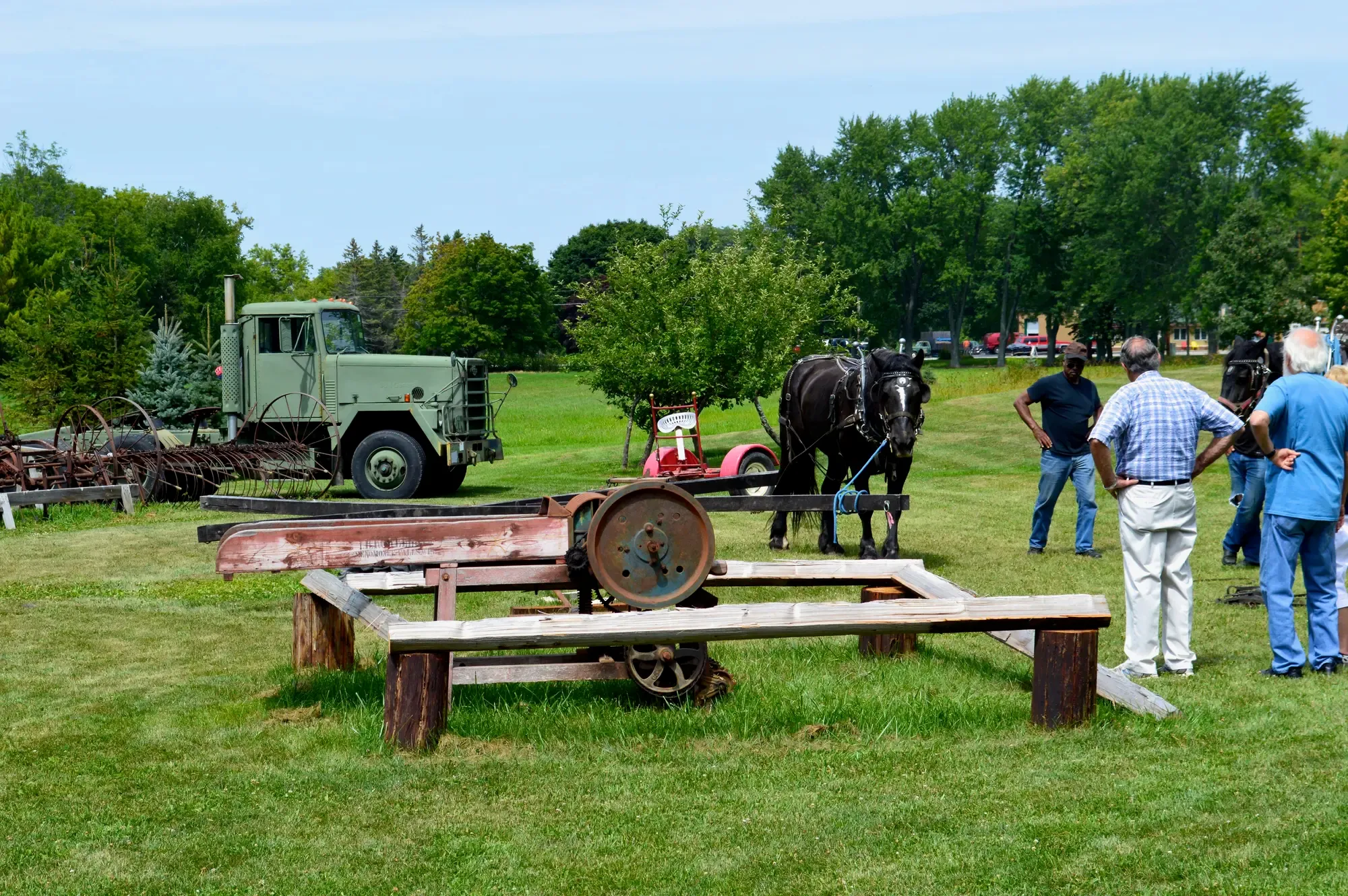 A draft horse in harness beside the antique sawmill rig and a vintage military truck