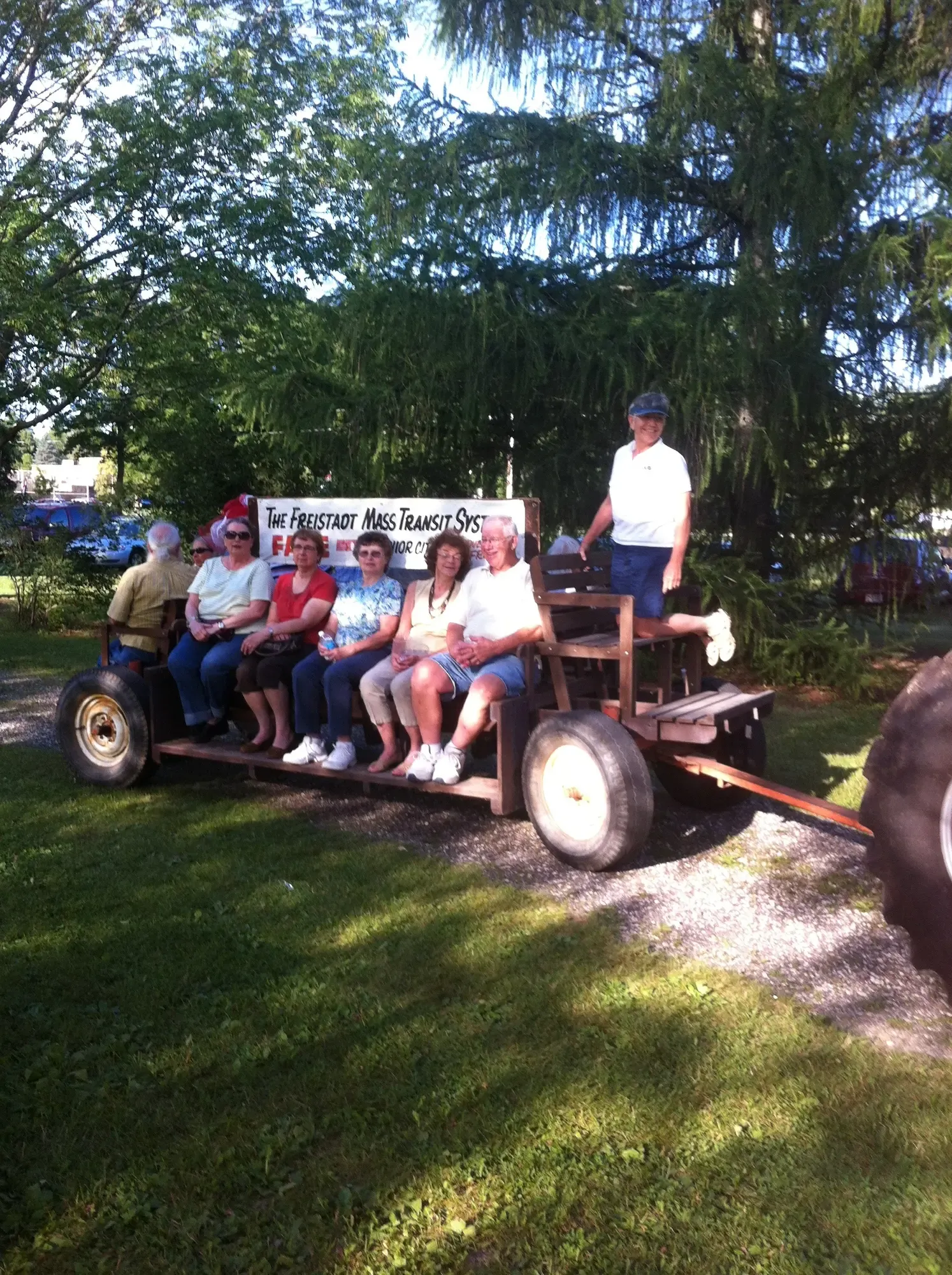 Members riding the bench wagon signed 'The Freistadt Mass Transit System' through the shade