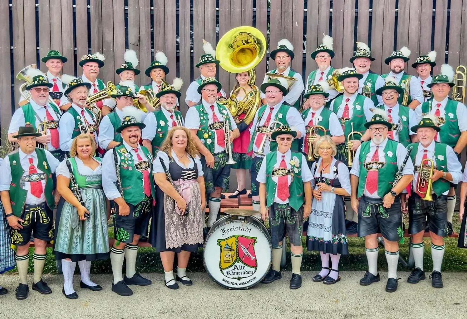 The Freistadt Alte Kameraden Band in green vests and feathered hats, instruments in hand around the band’s painted bass drum