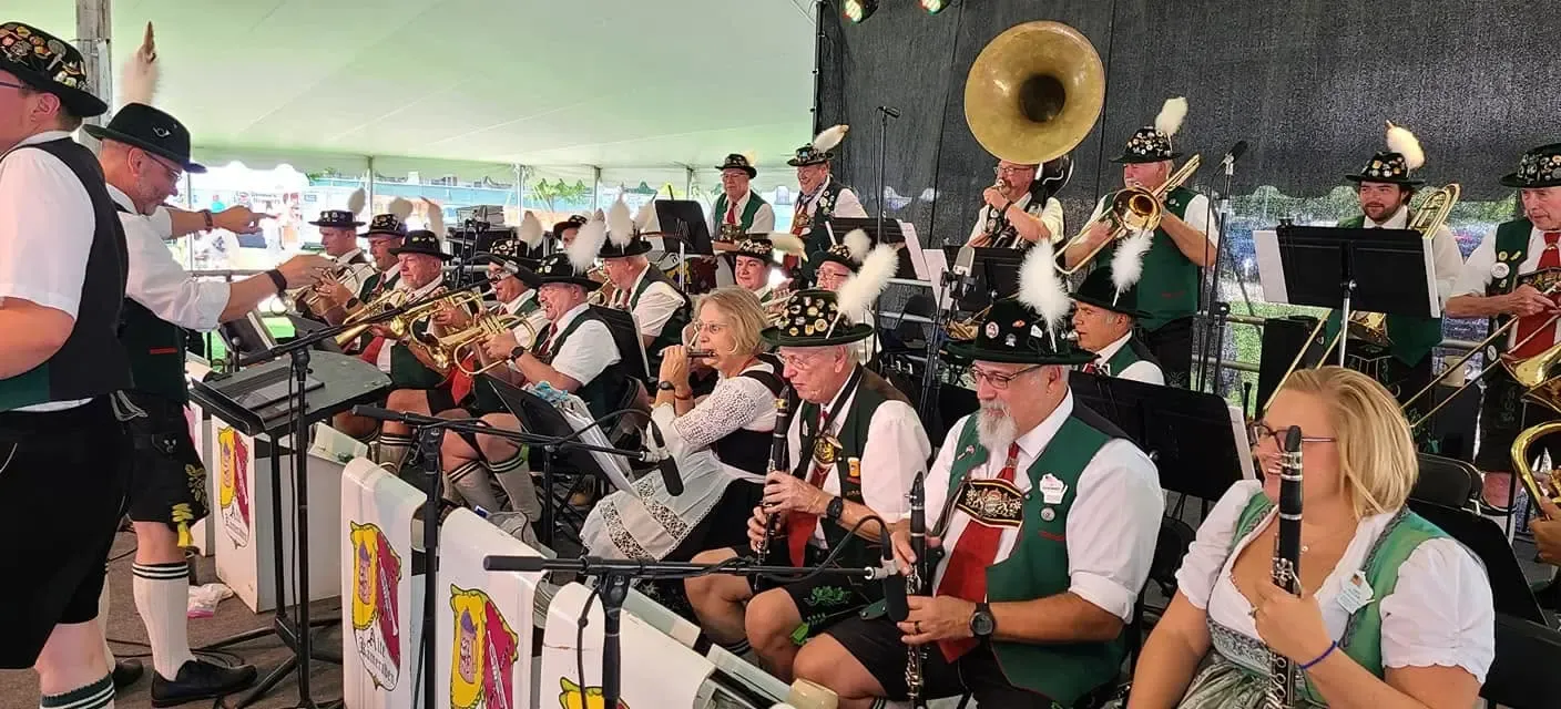 The Freistadt Alte Kameraden Band in Bavarian dress — feathered hats, lederhosen, and dirndls — playing brass and clarinets under a festival tent