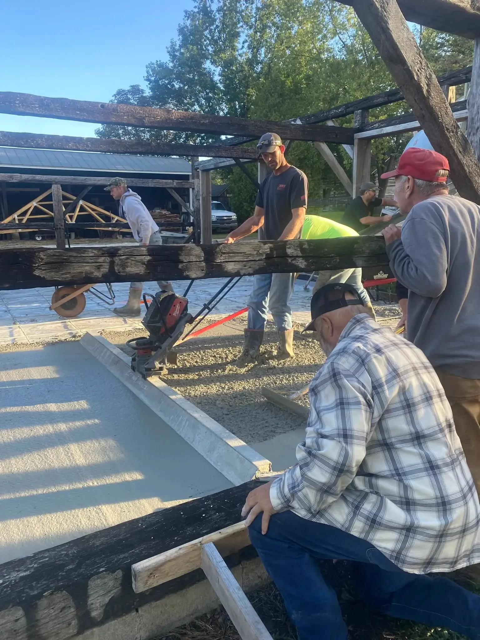 Volunteers leaning on a charred timber beam as the crew works the edge of the freshly poured concrete floor