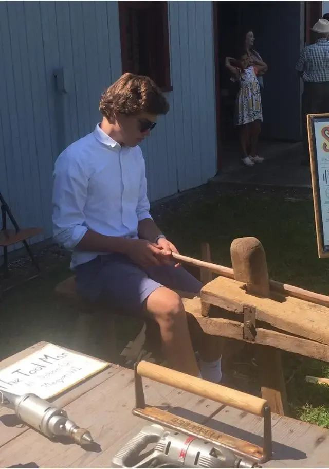 A young visitor shaping a piece of wood on the shaving horse at the Tool Man's bench