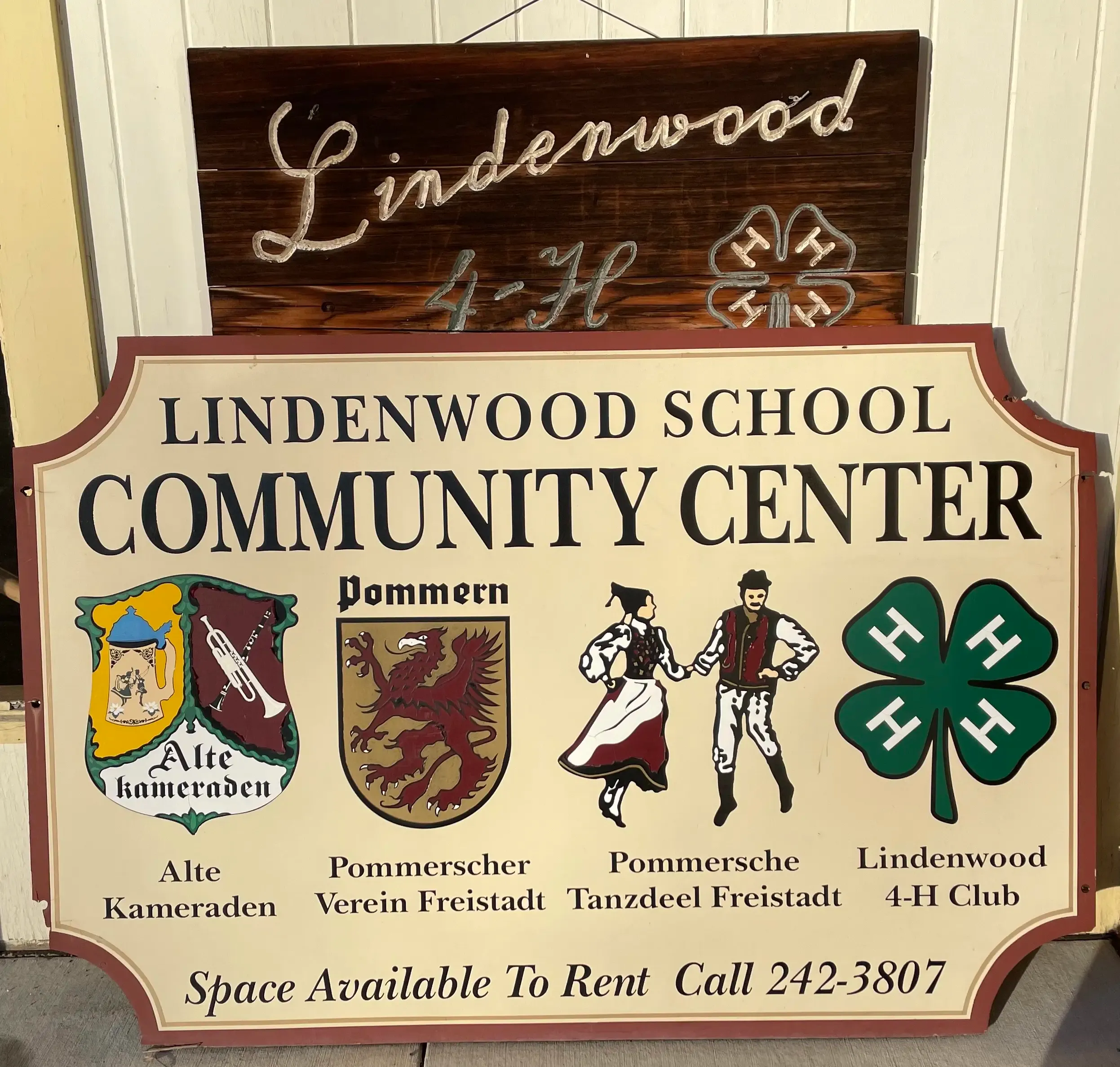 The Lindenwood School Community Center sign, with the emblems of the Alte Kameraden, Pommerscher Verein Freistadt, Pommersche Tanzdeel Freistadt, and Lindenwood 4-H Club