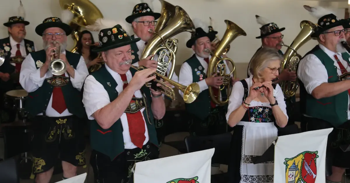 The Alte Kameraden band in feathered hats playing horns and trumpets at a festival