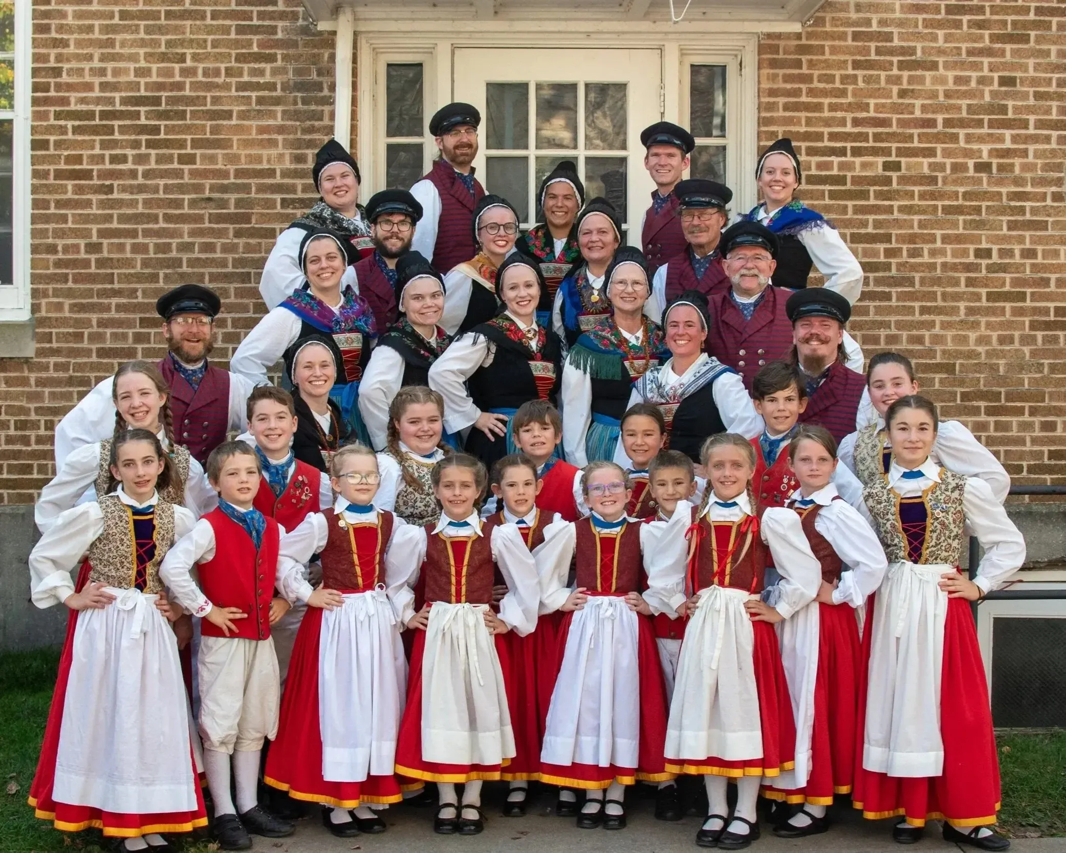 The full Pommersche Tanzdeel Freistadt troupe, from young children to adults, in Pomeranian folk costume on the schoolhouse steps