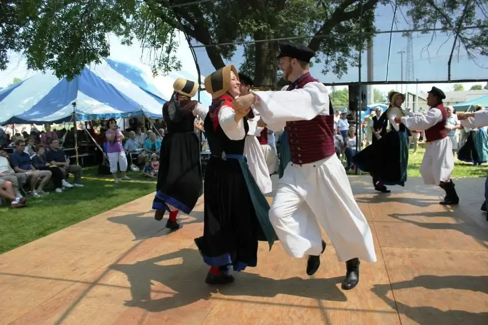 Couples in Pomeranian folk dress dancing on an outdoor stage at Pommerntag, the festival tent and crowd behind them