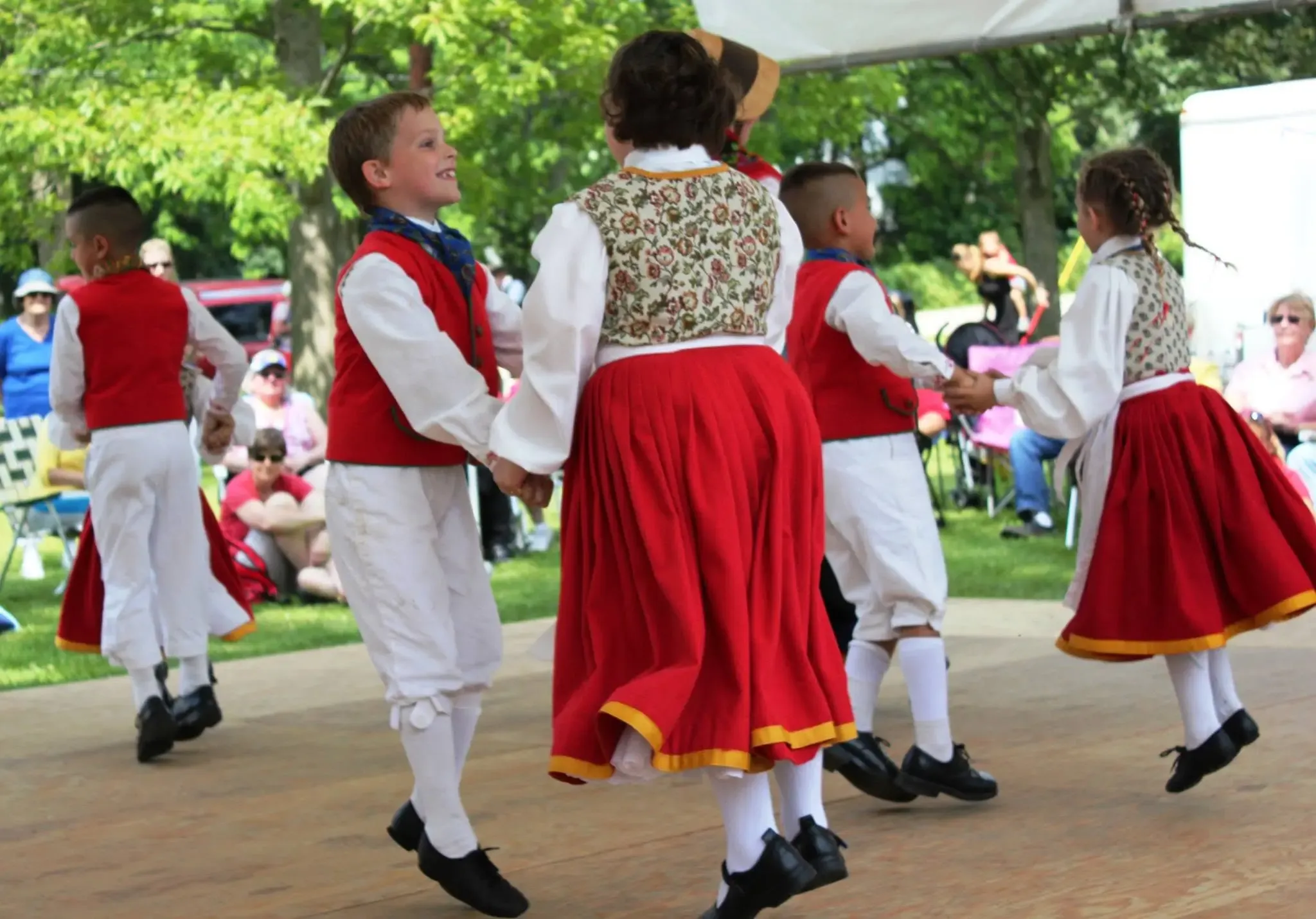 Children in Pomeranian folk dress dancing in pairs under the Pommerntag festival tent, spectators watching from the lawn