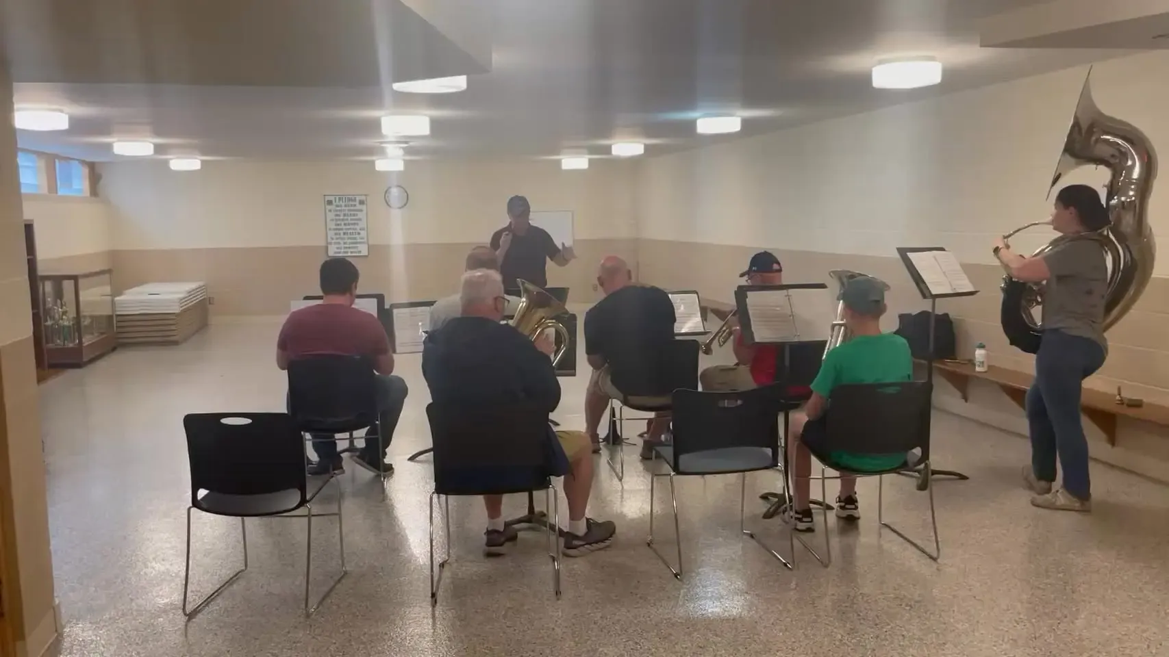 Musicians with tubas, trombones, and a sousaphone rehearsing in the church basement