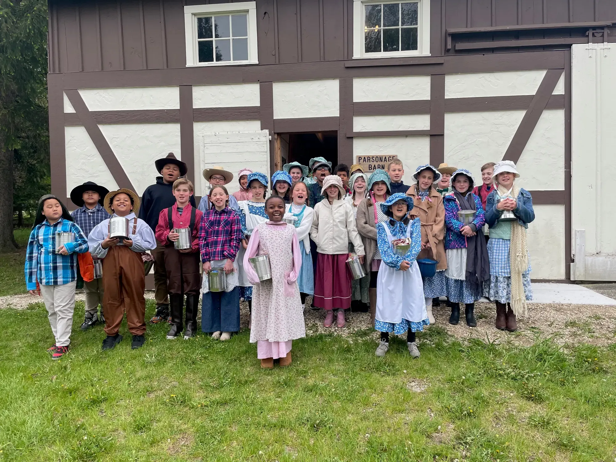 A fourth-grade class in bonnets and straw hats singing outside the Parsonage Barn