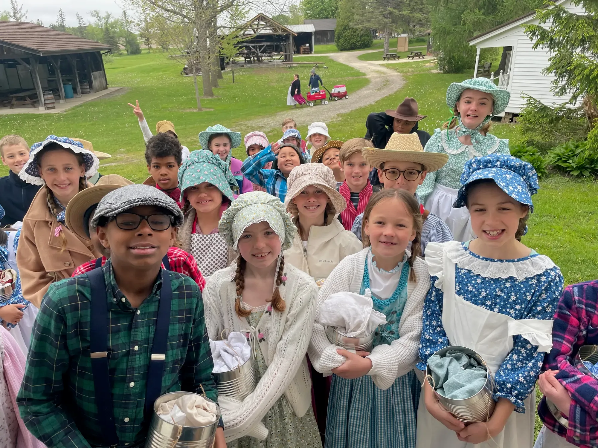 Fourth graders in bonnets and straw hats, tin-can pails in hand, gathered on the hill above the village grounds