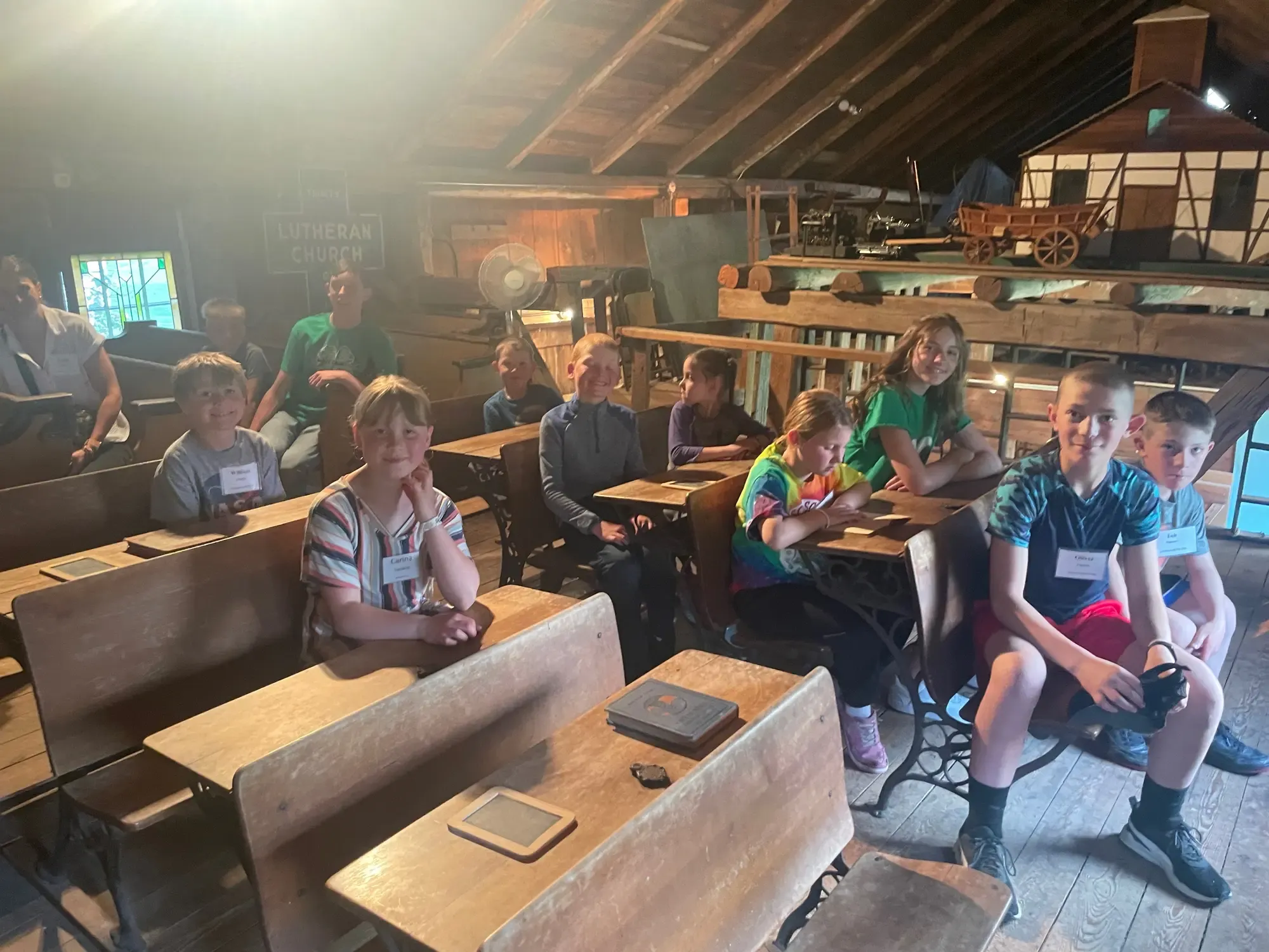 Summer visitors seated at the antique double desks in the historic schoolroom, slates at the ready