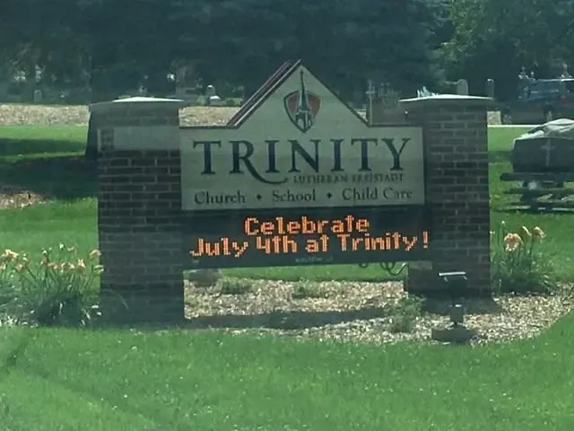 Brick Trinity sign on the lawn reading “Celebrate July 4th at Trinity!”