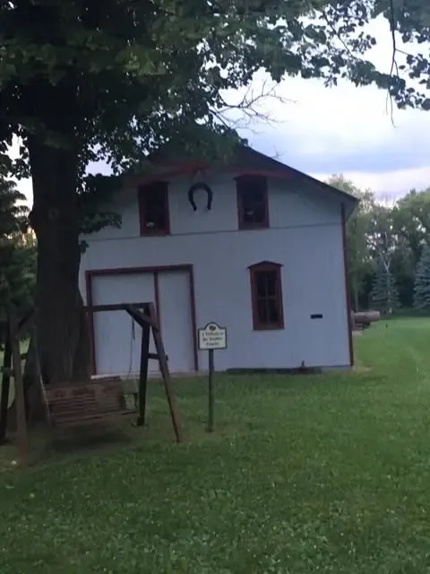 The white barn with red trim and a horseshoe over its door, a rope swing hanging beside it